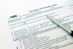 Tax Form 1065 on a white background with a silver pen resting on top.