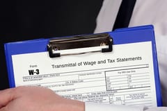 A tax professional holding a blue clip board with a W-3 form on top