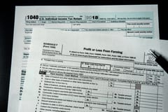 A Schedule F tax form sits on a table on top of a Form 1040. A pen rests on top of both forms.