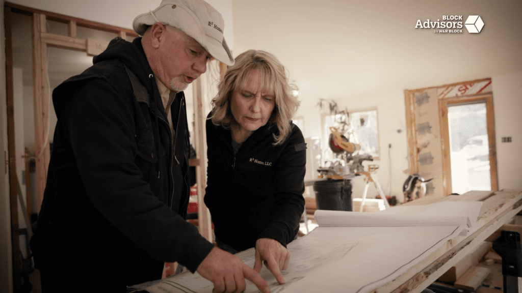 Jim Erickson and Leanne Knapp lean over a set of blueprints at a worksite for their company, R3 Homes