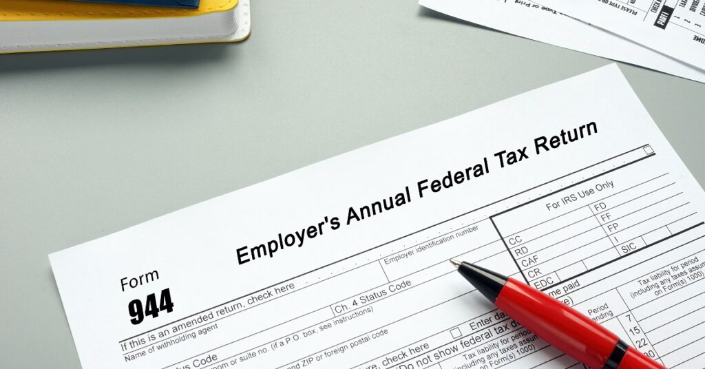 IRS Form 944 sitting on a table. A red pen is resting on top of the form.