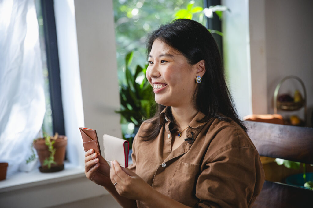 Heather Jiang, winner of a grant for women owned businesses, sitting holding up two wallets from her line of sustainable accessories made from reclaimed plant fibers.