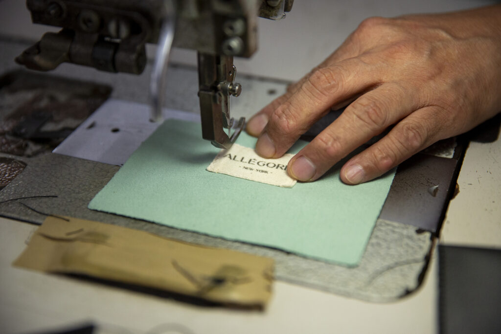 A worker sews an Allegorie label onto the lining of a bag.